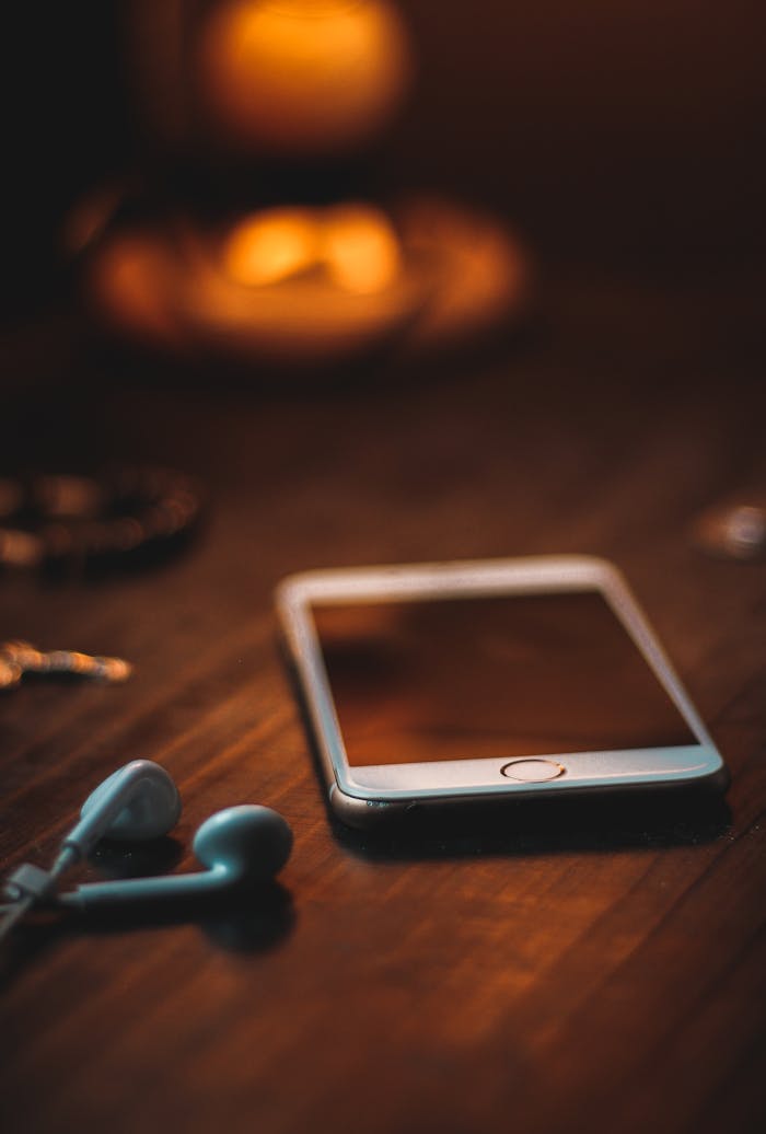 Home Mobile phone with earphones on a wooden table in warm ambient light, creating a cozy atmosphere.