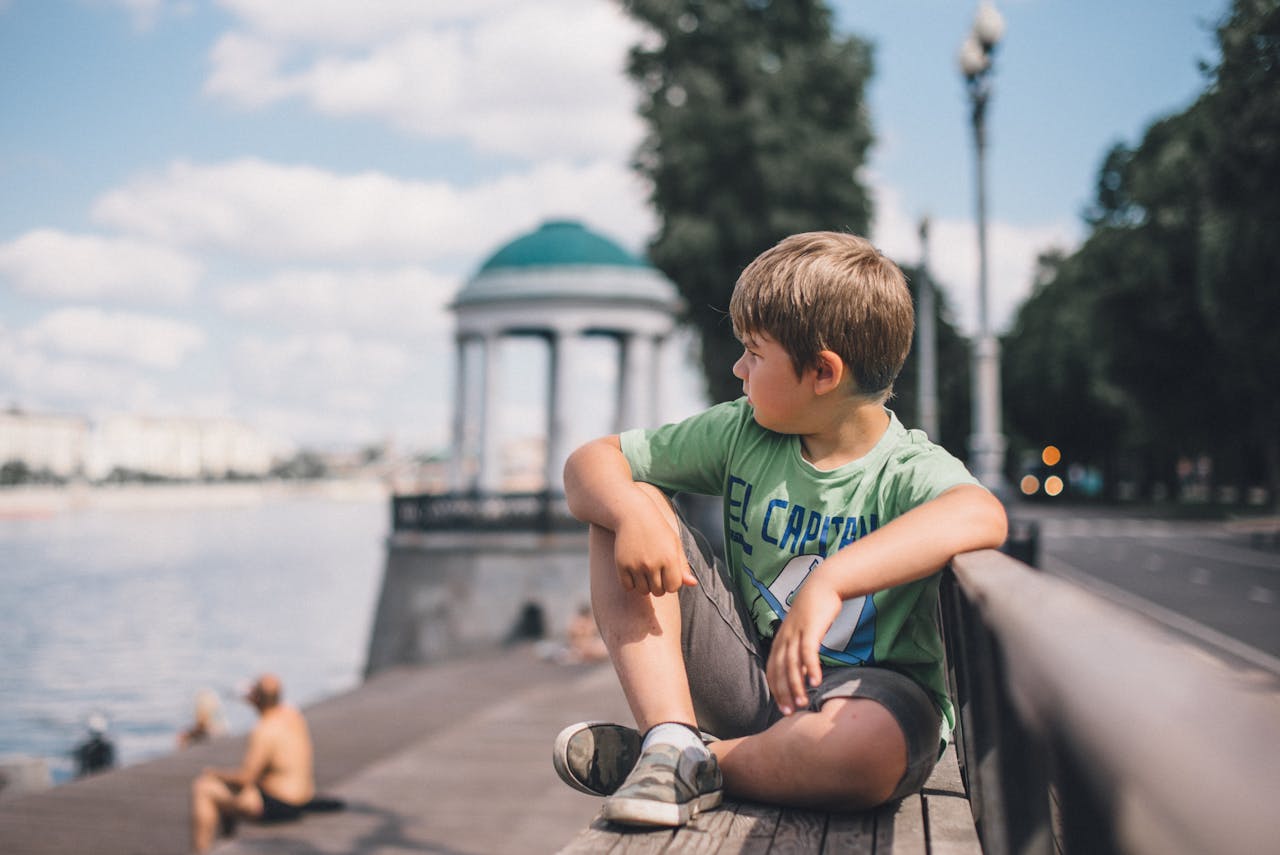 A young boy sitting on a riverside bench in Moscow, enjoying the summer day.